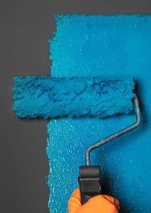 A roller applies blue paint to a dark grey surface.