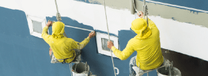 Painters suspended on rope seats prepare a building exterior for fresh paint.